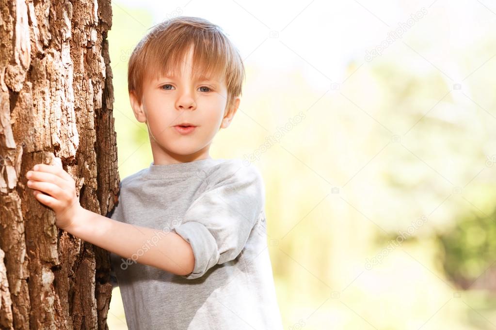 Little boy emerging from behind tree