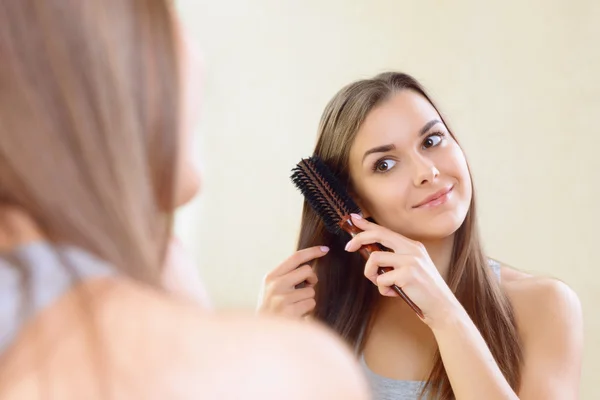 Meisje in spiegel haar haren kammen. — Stockfoto