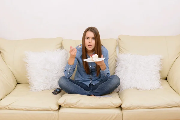 Девушка смотрит телевизор и ест на диване . — стоковое фото