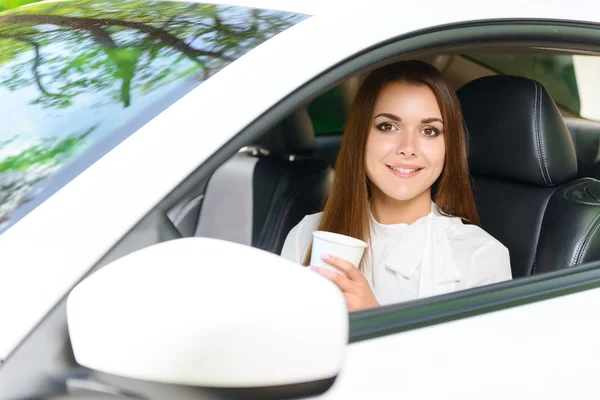 Smiling girl in car with cup of coffee — Stock Photo, Image