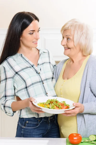 Par de mulheres segurando salada na cozinha — Fotografia de Stock