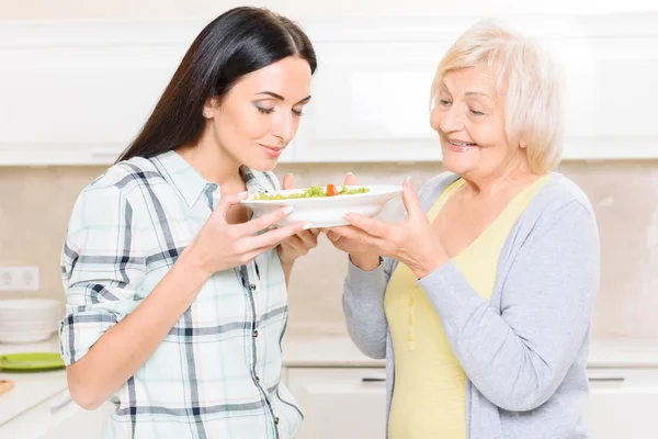 Granddaughter smelling salad in kitchen — Stock Photo, Image