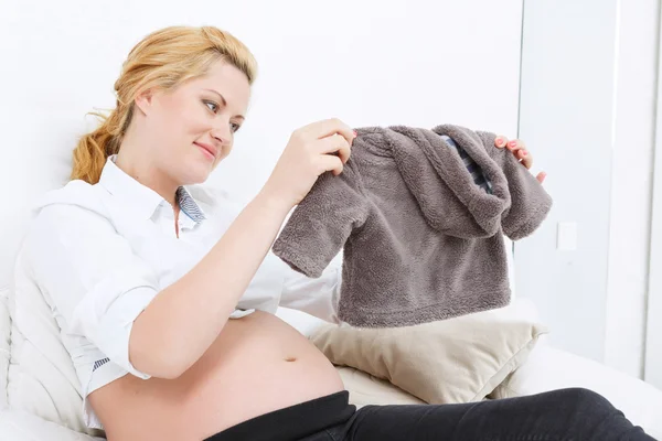 Pregnant woman holding baby clothes — Stock Photo, Image