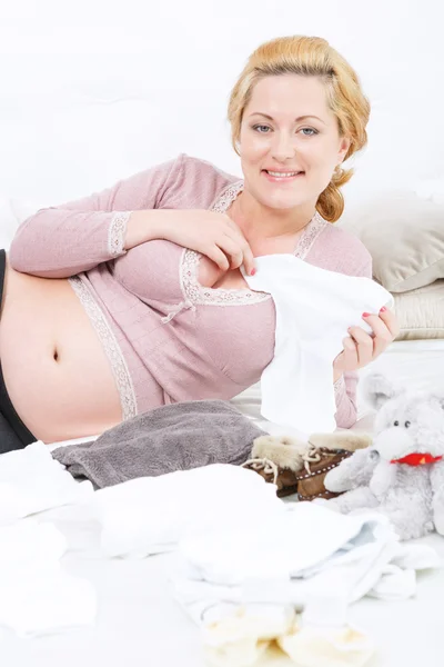 Pregnant woman holding baby clothes — Stock Photo, Image