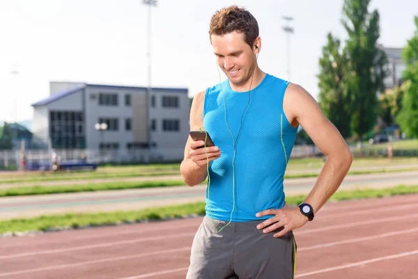 Stadyum üstünde hareket eden telefon ile ayakta sporcu — Stok fotoğraf