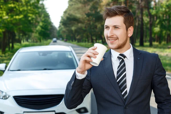 Businessman drinking coffee near car — Stock Photo, Image