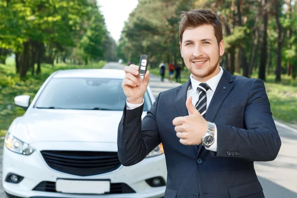 Businessman near car thumbing up with keys — Stock Photo, Image