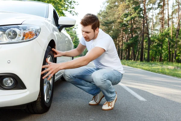Joven revisando el neumático de su coche —  Fotos de Stock