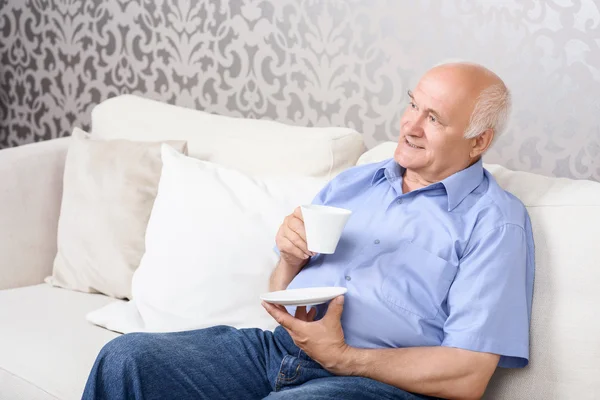 Старший мужчина сидит на диване с чашкой — стоковое фото