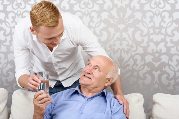 Grandson giving glass with water to grandfather — Stock Photo, Image