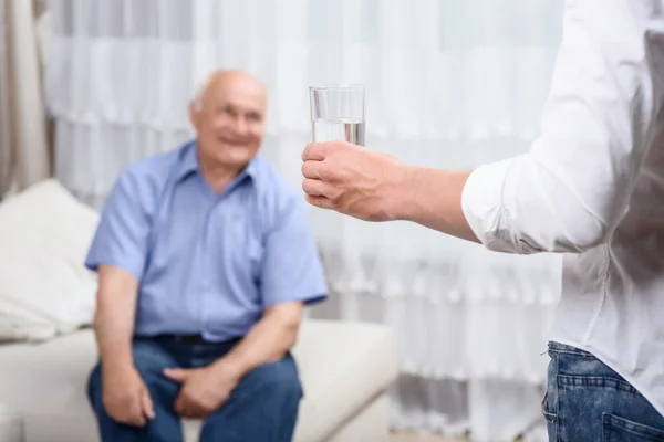 Junger Mann mit Glas Wasser in der Nähe des Großvaters — Stockfoto