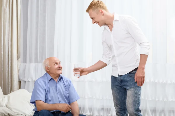 Nieto dando vaso con agua al abuelo —  Fotos de Stock