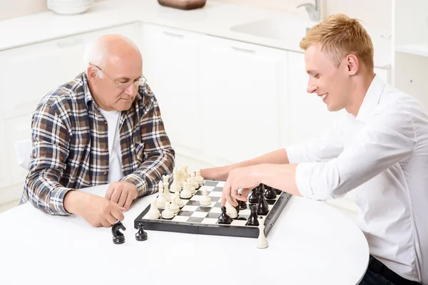 Grandson and grandfather playing chess in kitchen — Stock Photo, Image