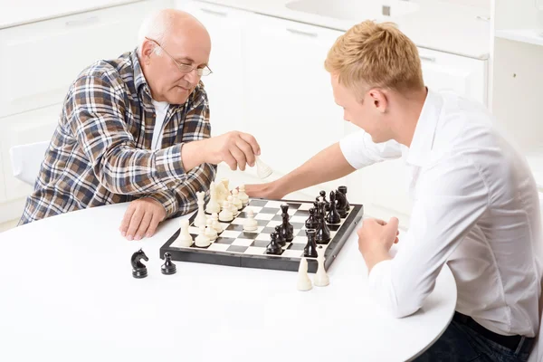 Neto e avô jogando xadrez na cozinha — Fotografia de Stock
