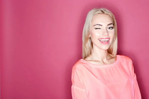 Hübsches lächelndes Mädchen zwinkert auf rosa Hintergrund — Stockfoto