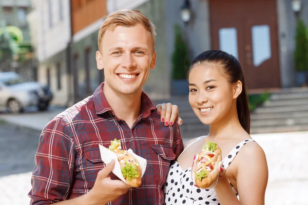 Ung man och kvinna med korv på gatan — Stockfoto