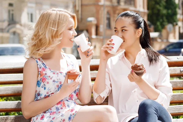 Två väninnor i park med kaffe och cupcakes — Stockfoto