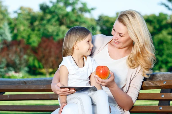 Mãe usando tablet no banco com a filha — Fotografia de Stock