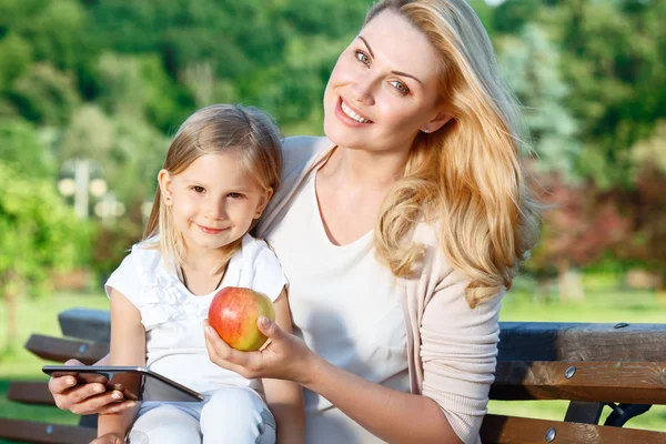 Mother using tablet on bench with daughter — Stock Photo, Image