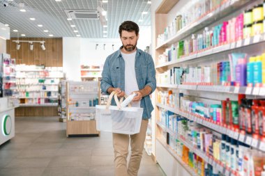 Sakallı adam eczanede doğru sağlık ürünlerini arıyor.