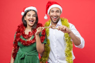 Noel Baba şapkaları takan neşeli aile Noel 'i süslerle ve şeker kamışlarıyla kutluyor. Kırmızı arka planda izole edilmiş tatil neşesinin tadını çıkarıyorlar.