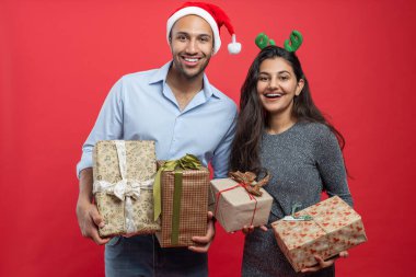 Mutlu çift Noel 'i şenlikli şapkalar ve hediye kutularıyla kutluyor. Kırmızı arka plandaki partide arkadaşlarını kutluyor.