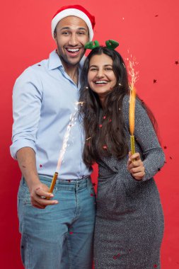 Neşeli kadın ve erkek birlikte yeni yılı kutluyorlar. Kırmızı arka planda izole edilmiş neşeli kıvılcımlar tutuyorlar.