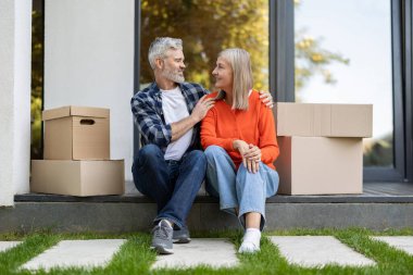 Sundurmanın yanında oturan yaşlı çift taşındıktan sonra gülümsüyor ve dinleniyor.