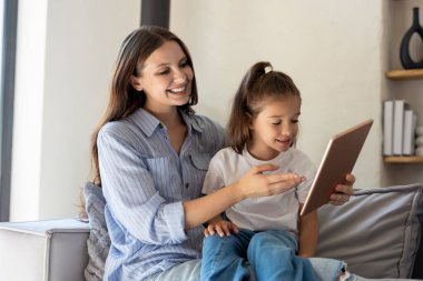 Anne ve çocuk kanepede oturuyorlar ve ellerinde dijital tablet var.
