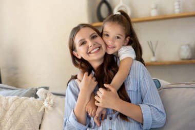 Neşeli anne ve kız evdeki kanepede oturup sarılıyorlar.