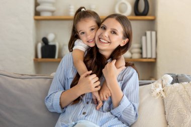 Kanepede birlikte vakit geçirirken annesinin yanına yaslanan gülümseyen kızın portresi.