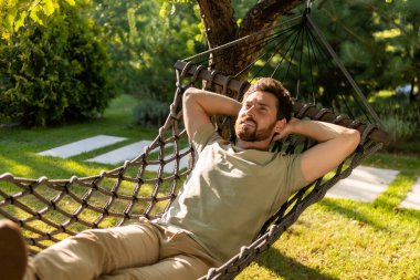 Rahatlama. Sakallı genç adam bir hamakta yatıyor ve rahatlamış hissediyor.