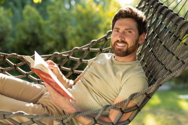 Açık havada okumak. Kafkas sakallı genç adam elinde bir kitapla hamakta yatıyor.