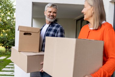 Gülümseyen yaşlı çift, evin girişinde karton kutular taşıyorlar.