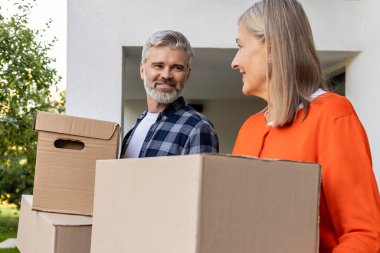 Gülümseyen olgun bir çift yeni eve karton kutular taşıyor.