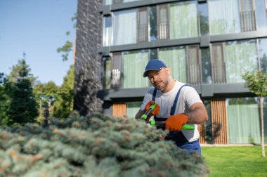 Çağdaş apartman kompleksinin avlusunda yeşil manzarayı koruyan üniformalı bir işçi.