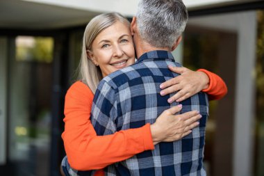 Şefkatle sarılın. Turuncu gömlekli uzun saçlı kadın kocasını kucaklıyor.