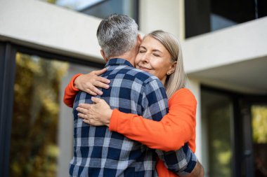 Şefkatle sarılın. Turuncu gömlekli uzun saçlı kadın kocasını kucaklıyor.
