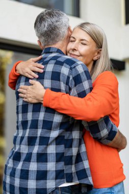 Şefkatle sarılın. Turuncu gömlekli uzun saçlı kadın kocasını kucaklıyor.