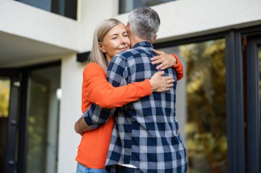 Şefkatle sarılın. Turuncu gömlekli uzun saçlı kadın kocasını kucaklıyor.