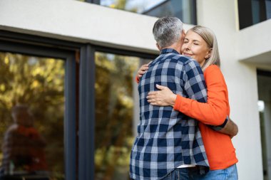 Şefkatle sarılın. Turuncu gömlekli uzun saçlı kadın kocasını kucaklıyor.
