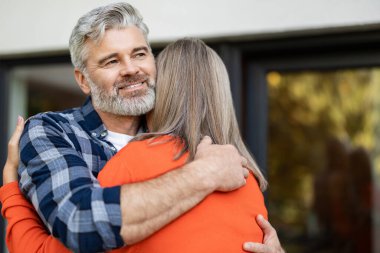 Şefkatle sarılın. Turuncu gömlekli uzun saçlı kadın kocasını kucaklıyor.
