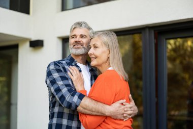 Sarılalım. Gri saçlı sakallı adam karısına sarılıyor ve mutlu bir şekilde gülümsüyor.