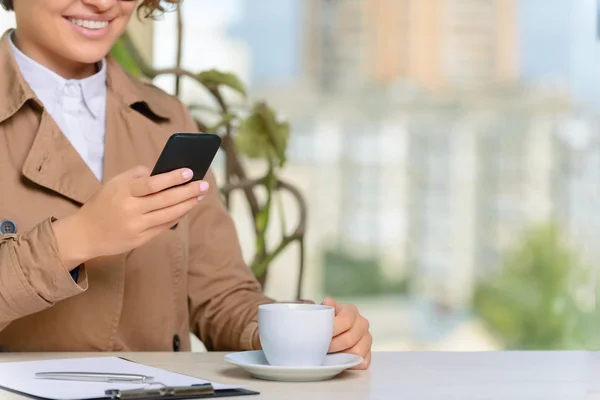 Mujer sosteniendo móvil y bebiendo café — Foto de Stock