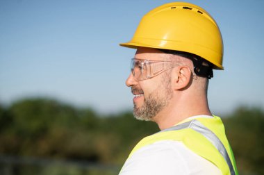 Sarı kask takan erkek teknisyen portresi mavi, sinsi arka planda poz veriyor.