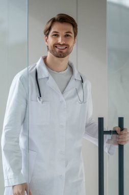 Kirli sakallı ve laboratuvar önlüklü doktor cam kapıdan geçerken mutlu.
