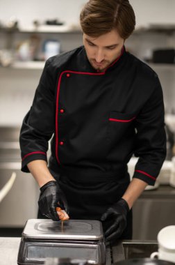 Profesyonel aşçı, somon parçalarını mutfak ölçeğinde tartıyor.