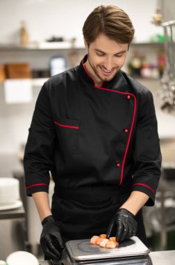 Siyah üniformalı şef somon balığını tartıyor.