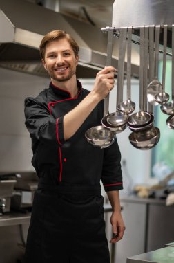 Lokanta mutfağında çalışan kendinden emin, siyah üniformalı bir aşçı.