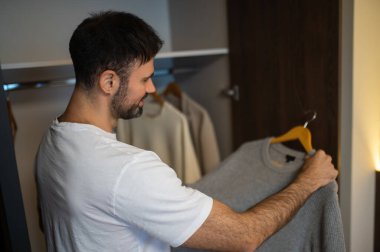 Adam kıyafetlerini kontrol ediyor. Koyu saçlı beyaz bir adam oteldeki gardıropta kıyafetlerini kontrol ediyor.
